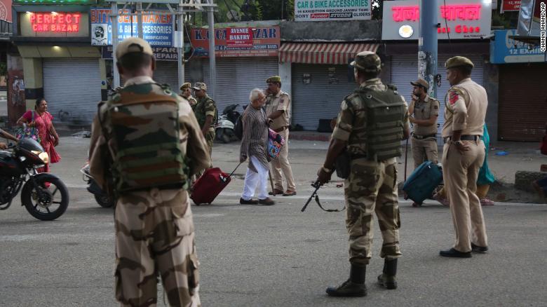 Tourists walk past Indian security forces during curfew like restrictions in Jammu, India, Monday, Aug. 5, 2019. An indefinite security lockdown was in place in the Indian-controlled portion of divided Kashmir on Monday, stranding millions in their homes as authorities also suspended some internet services and deployed thousands of fresh troops around the increasingly tense region. (AP Photo/Channi Anand)